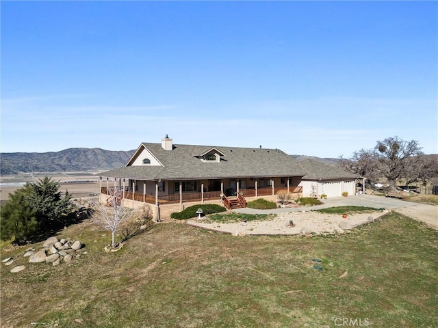 rear view of house with a porch, an attached garage, a mountain view, a yard, and driveway