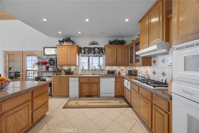 kitchen featuring stone countertops, under cabinet range hood, white appliances, french doors, and glass insert cabinets