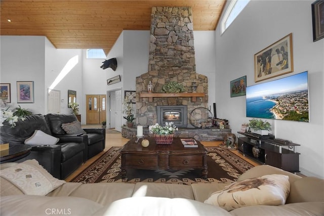 living room featuring wood ceiling, a stone fireplace, and a high ceiling