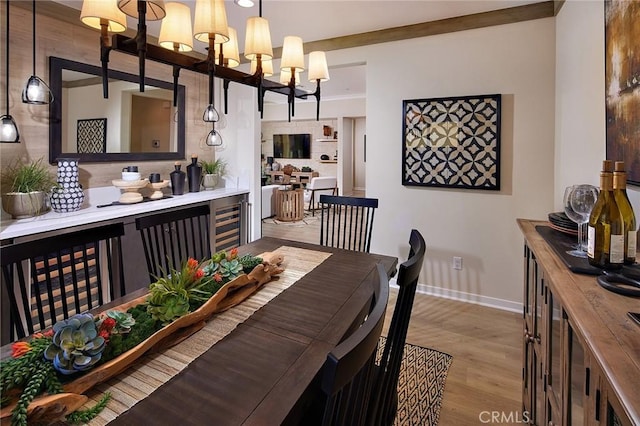 dining space featuring wine cooler, crown molding, light wood-style floors, a chandelier, and baseboards