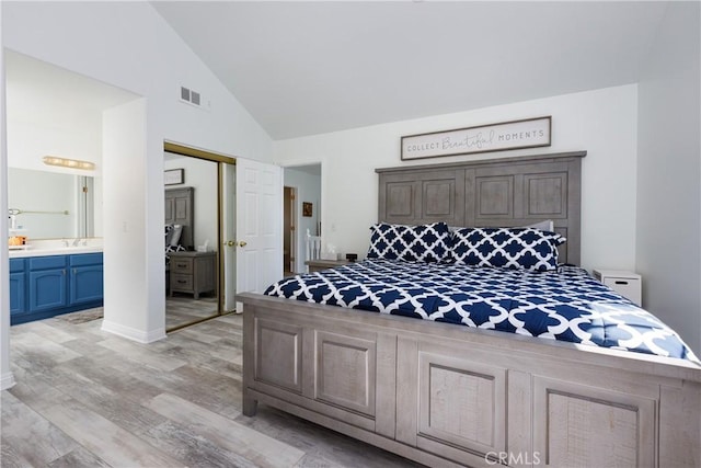 bedroom with light wood finished floors, visible vents, connected bathroom, high vaulted ceiling, and a closet