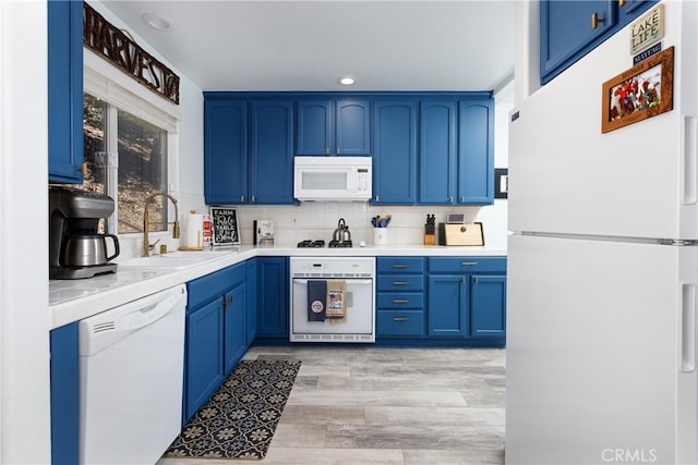 kitchen with white appliances, a sink, light countertops, blue cabinetry, and backsplash