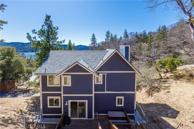 rear view of property featuring a shingled roof and a chimney