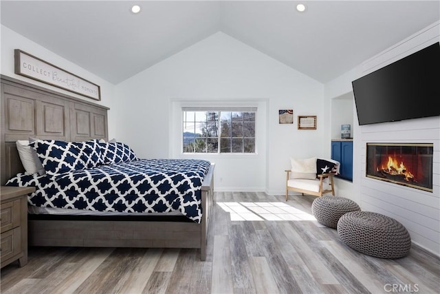 bedroom with lofted ceiling, recessed lighting, a glass covered fireplace, and light wood-style floors