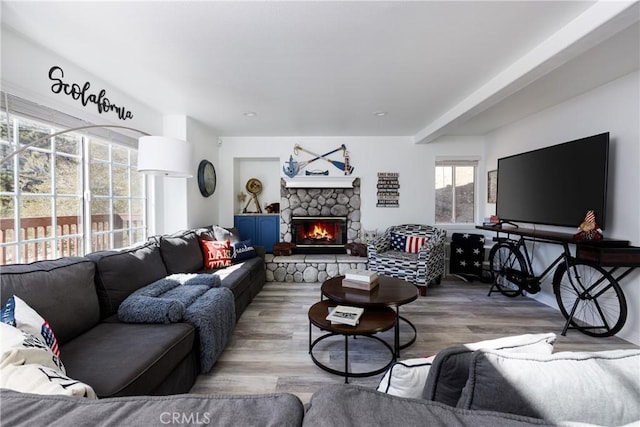 living area featuring a stone fireplace, beam ceiling, and wood finished floors
