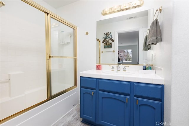full bath featuring vanity, visible vents, enclosed tub / shower combo, and wood finished floors