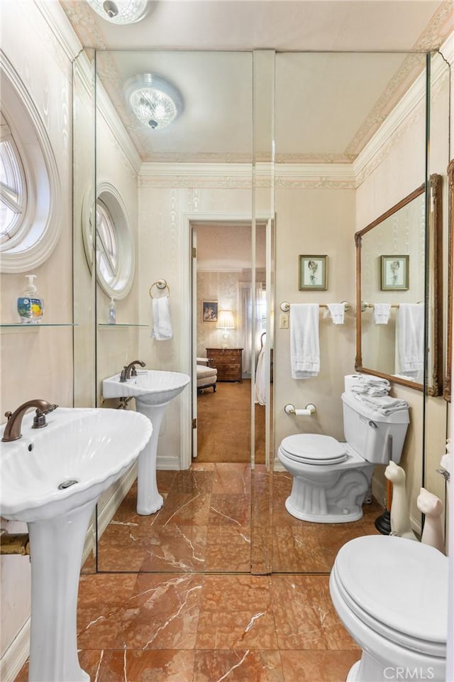 bathroom featuring marble finish floor, crown molding, toilet, two sinks, and ensuite bath