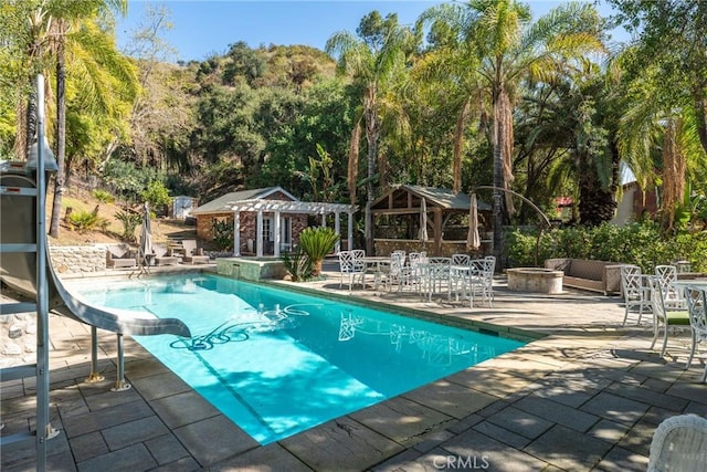 outdoor pool featuring an outdoor fire pit, an outbuilding, a storage structure, a water slide, and a patio area