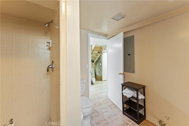 bathroom with electric panel, a tile shower, and toilet