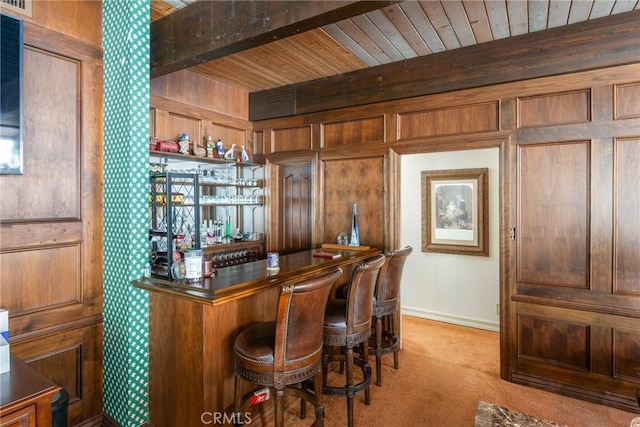 bar with beam ceiling, light carpet, wooden walls, a bar, and wooden ceiling