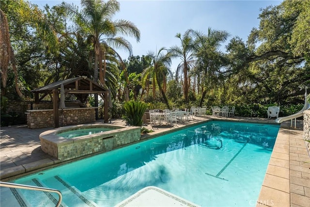 pool with a water slide, a patio, a gazebo, and an in ground hot tub