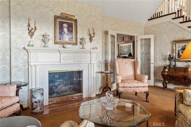 carpeted living area featuring wallpapered walls, baseboards, a glass covered fireplace, lofted ceiling, and stairs