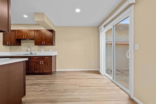 kitchen featuring light wood finished floors, recessed lighting, light countertops, a sink, and baseboards