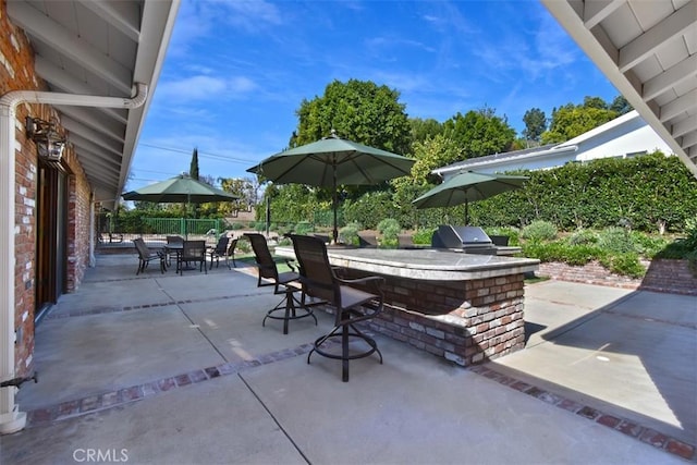 view of patio / terrace featuring exterior bar, a grill, fence, and an outdoor kitchen