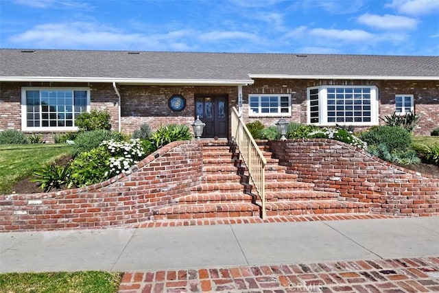 ranch-style home with a shingled roof, stairway, and brick siding