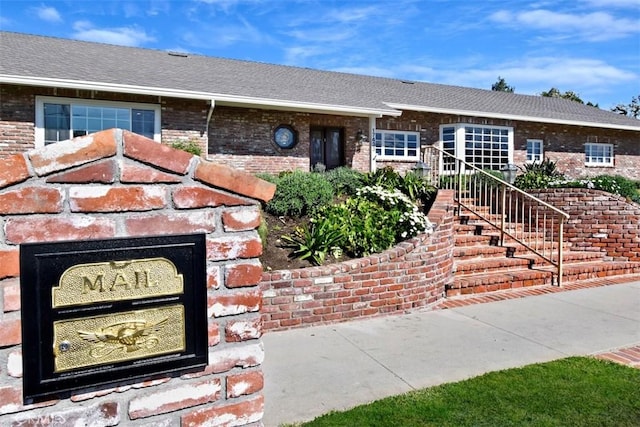 ranch-style house with a shingled roof, brick siding, and stairs