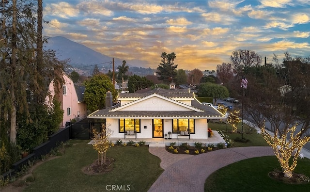 view of front of home featuring a porch, fence, decorative driveway, a mountain view, and a front lawn