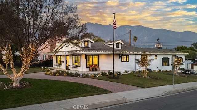 view of front of property featuring a front lawn, decorative driveway, a porch, and a mountain view