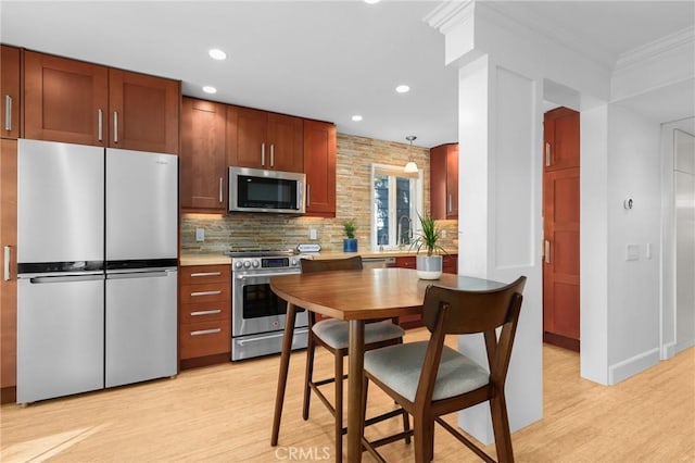 kitchen with light wood-style floors, light countertops, appliances with stainless steel finishes, hanging light fixtures, and crown molding