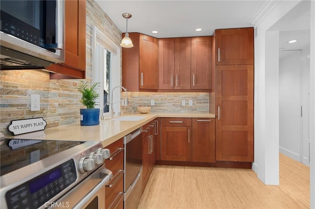 kitchen with stainless steel appliances, a sink, light countertops, hanging light fixtures, and light wood-type flooring