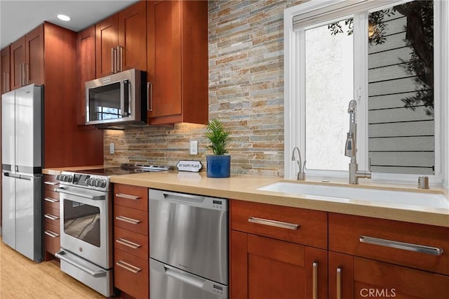 kitchen featuring light wood finished floors, decorative backsplash, appliances with stainless steel finishes, light countertops, and a sink