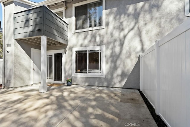 rear view of house with a patio area, fence, and stucco siding