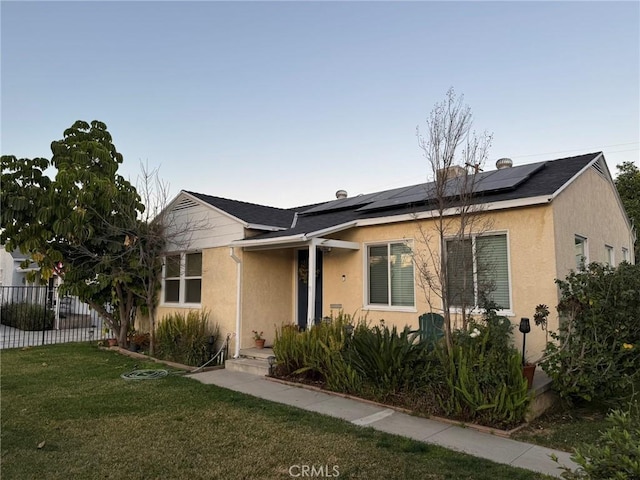 view of front of house with a front yard, stucco siding, fence, and solar panels