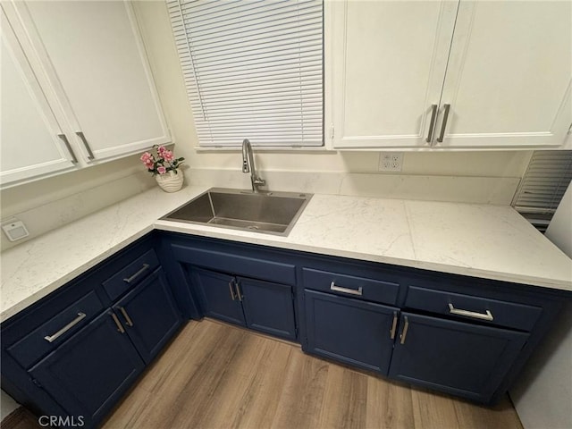 kitchen with light wood finished floors, white cabinets, light stone counters, blue cabinetry, and a sink