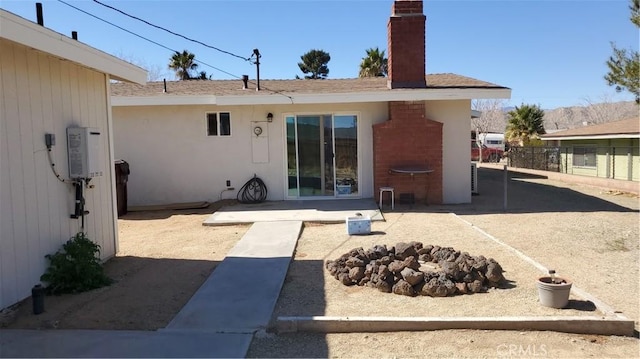 rear view of house featuring stucco siding, a patio, a chimney, and fence