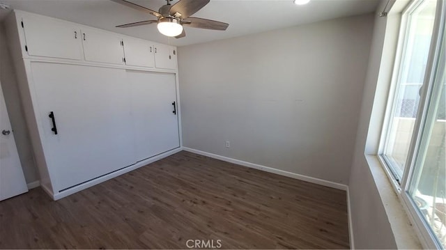 unfurnished bedroom featuring dark wood-style floors, multiple windows, a closet, and baseboards