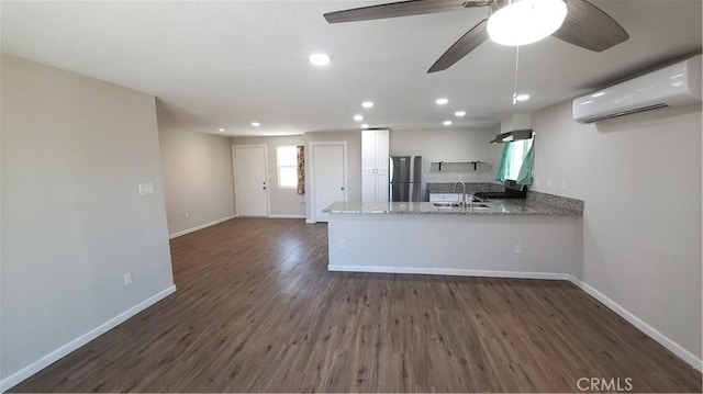 kitchen with a wall unit AC, a peninsula, baseboards, white cabinets, and freestanding refrigerator