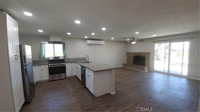 kitchen featuring a wall unit AC, stainless steel appliances, open floor plan, white cabinetry, and a peninsula