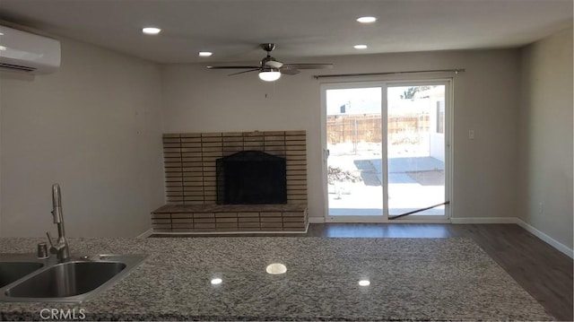 unfurnished living room featuring dark wood-style floors, a brick fireplace, an AC wall unit, a sink, and ceiling fan