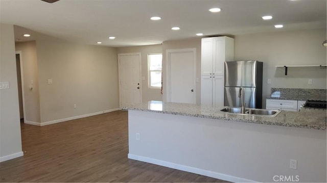 kitchen featuring light stone counters, a sink, freestanding refrigerator, and white cabinetry