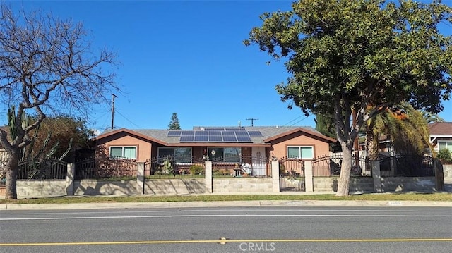 ranch-style home with a fenced front yard, stucco siding, a gate, and roof mounted solar panels