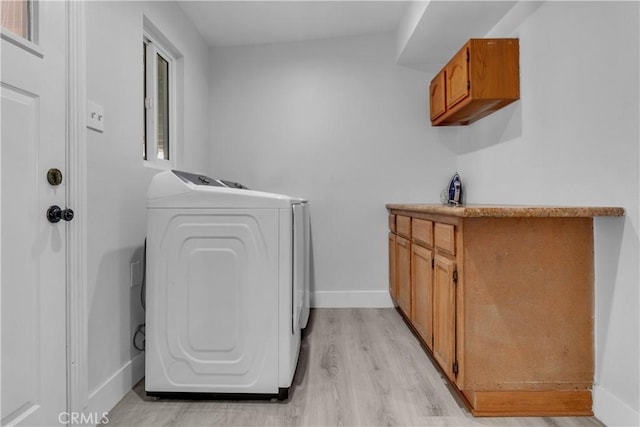 clothes washing area with light wood-style floors, baseboards, cabinet space, and washing machine and clothes dryer