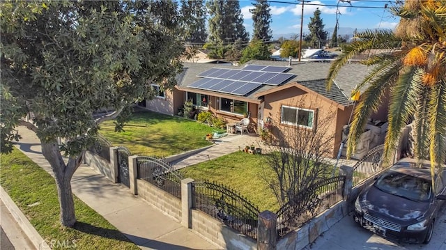 ranch-style home with a fenced front yard, a shingled roof, roof mounted solar panels, stucco siding, and a front lawn