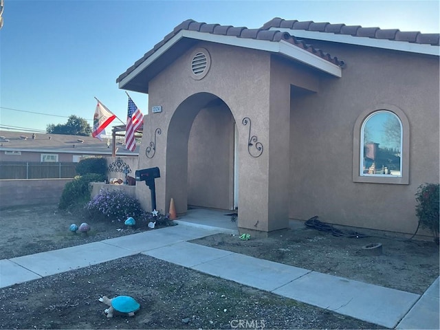 view of front of home featuring fence, a tile roof, and stucco siding