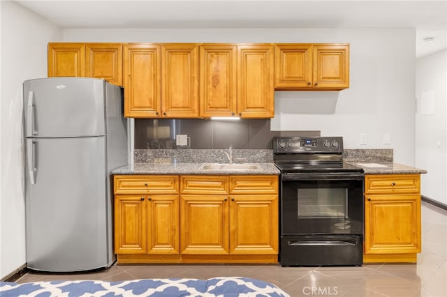 kitchen featuring stone counters, light tile patterned floors, black range with electric stovetop, freestanding refrigerator, and a sink