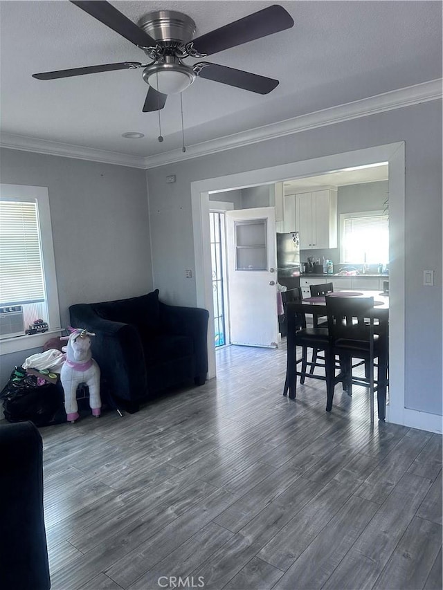 living room featuring cooling unit, wood finished floors, a ceiling fan, and crown molding