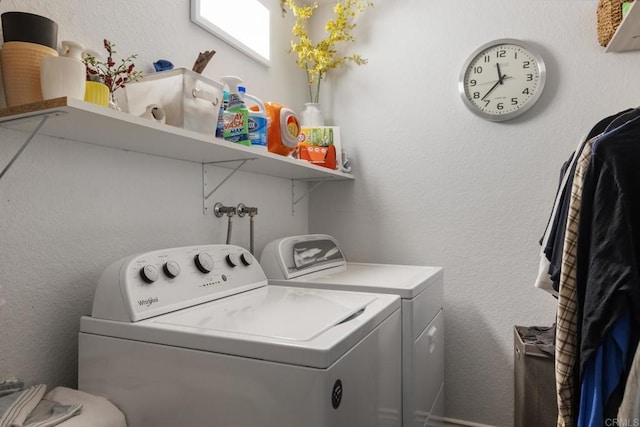 clothes washing area featuring a textured wall, laundry area, and washer and clothes dryer