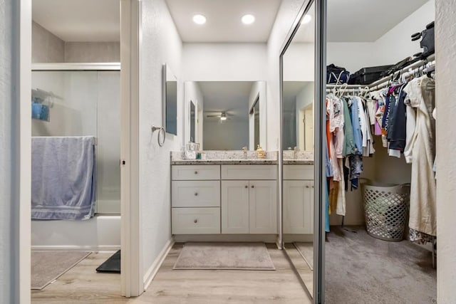 bathroom with a walk in closet, bath / shower combo with glass door, vanity, wood finished floors, and baseboards