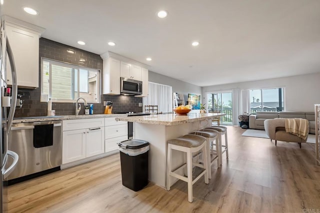 kitchen featuring stainless steel appliances, a kitchen island, white cabinets, open floor plan, and a kitchen bar