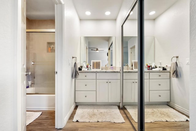 bathroom featuring baseboards, bath / shower combo with glass door, wood finished floors, and vanity