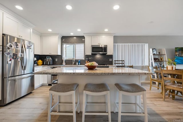 kitchen with stainless steel appliances, a center island, white cabinetry, and light stone countertops