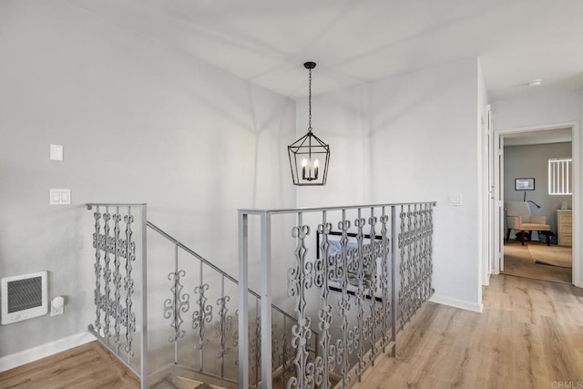 hallway featuring baseboards, wood finished floors, heating unit, an inviting chandelier, and an upstairs landing