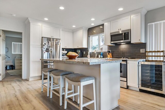 kitchen with beverage cooler, a breakfast bar, a kitchen island, white cabinets, and appliances with stainless steel finishes