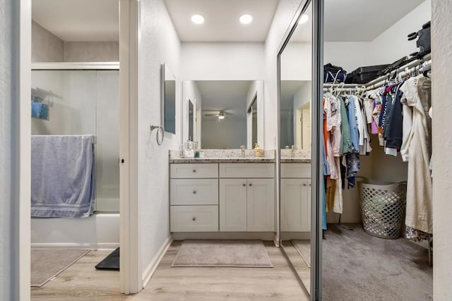 full bath featuring baseboards, bath / shower combo with glass door, wood finished floors, a spacious closet, and vanity