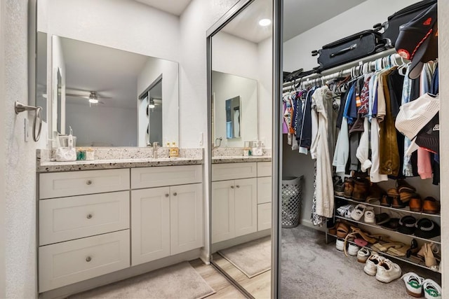 bathroom with a spacious closet, vanity, and a ceiling fan