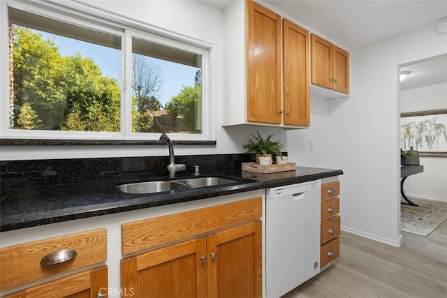 kitchen featuring brown cabinetry, dishwasher, dark stone countertops, light wood-type flooring, and a sink